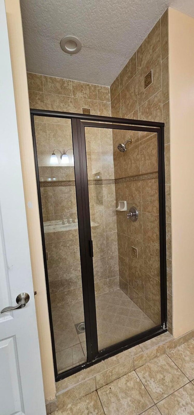 bathroom with a textured ceiling, tile patterned flooring, and an enclosed shower