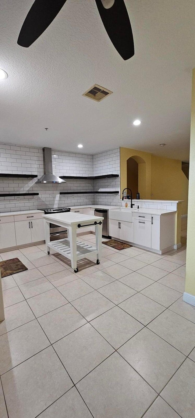 kitchen with light tile patterned floors, white cabinetry, decorative backsplash, and wall chimney range hood