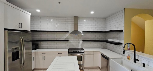 kitchen featuring white cabinetry, stainless steel appliances, backsplash, wall chimney exhaust hood, and sink