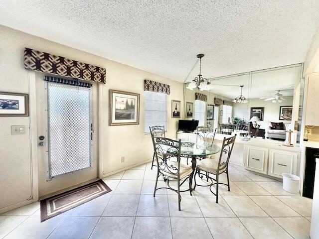 tiled dining space featuring ceiling fan with notable chandelier and a textured ceiling