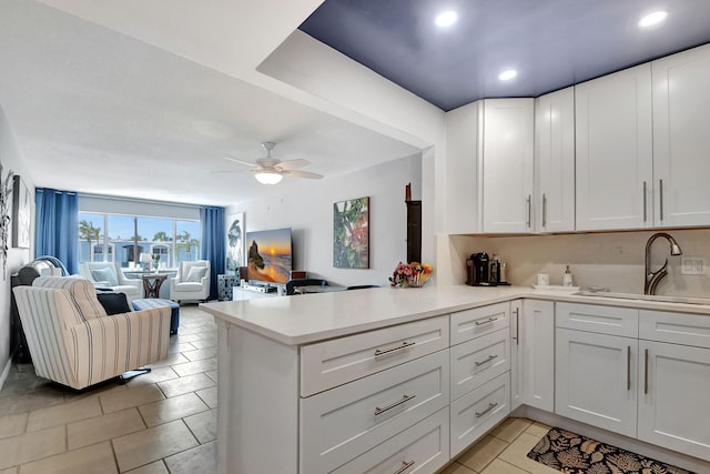 kitchen with kitchen peninsula, ceiling fan, sink, light tile patterned floors, and white cabinetry