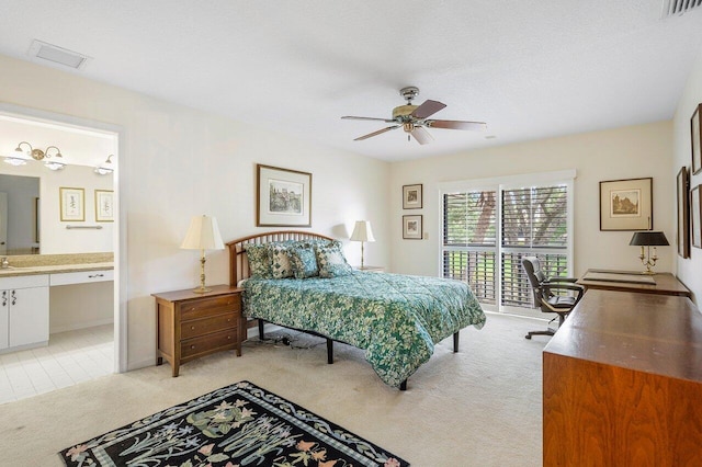 bedroom with ceiling fan, light colored carpet, a textured ceiling, and ensuite bath