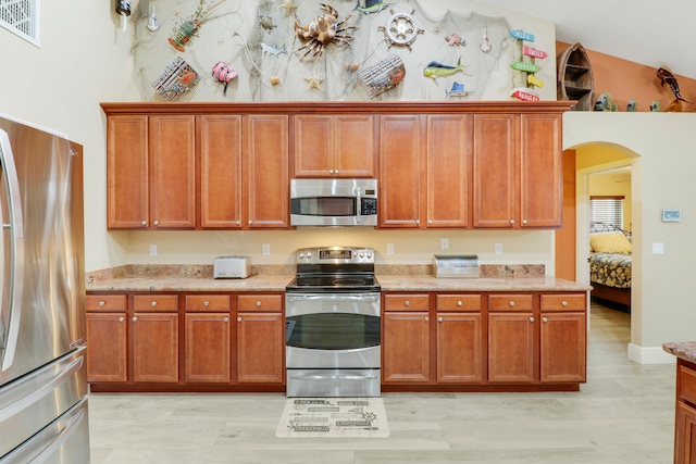 kitchen featuring appliances with stainless steel finishes, vaulted ceiling, light stone countertops, and light wood-type flooring