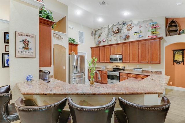 kitchen featuring light hardwood / wood-style floors, a kitchen bar, kitchen peninsula, and stainless steel appliances