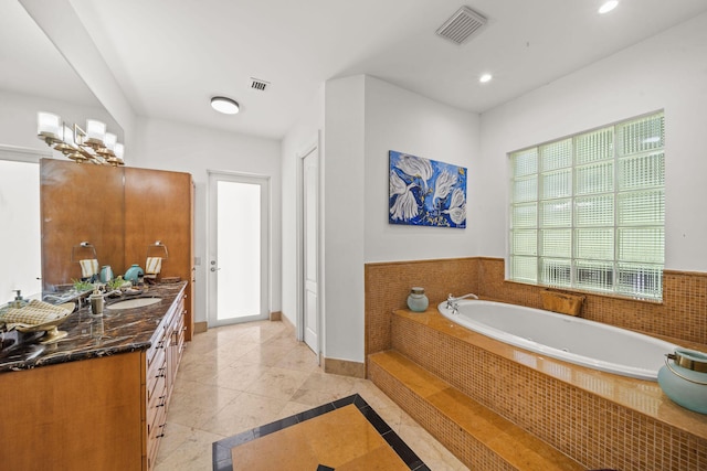 bathroom featuring tile patterned flooring, vanity, and tiled bath