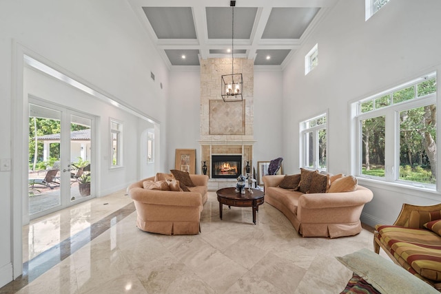 living room featuring a fireplace, french doors, a towering ceiling, and a notable chandelier