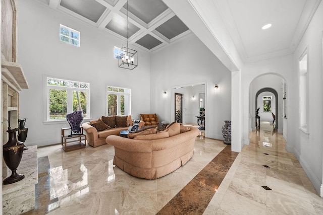 living room with a notable chandelier, a towering ceiling, crown molding, and coffered ceiling