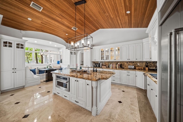 kitchen with dark stone counters, wood ceiling, a kitchen island with sink, decorative light fixtures, and white cabinetry