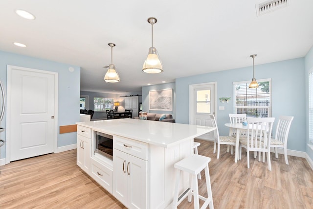 kitchen with built in microwave, a center island, white cabinets, and decorative light fixtures