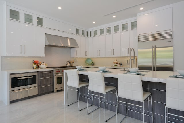 kitchen with white cabinetry, a breakfast bar area, tasteful backsplash, wall chimney exhaust hood, and high end appliances