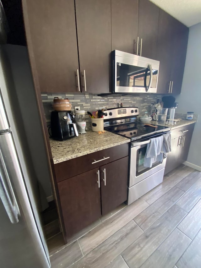 kitchen with stainless steel appliances, tasteful backsplash, light stone counters, and dark brown cabinets