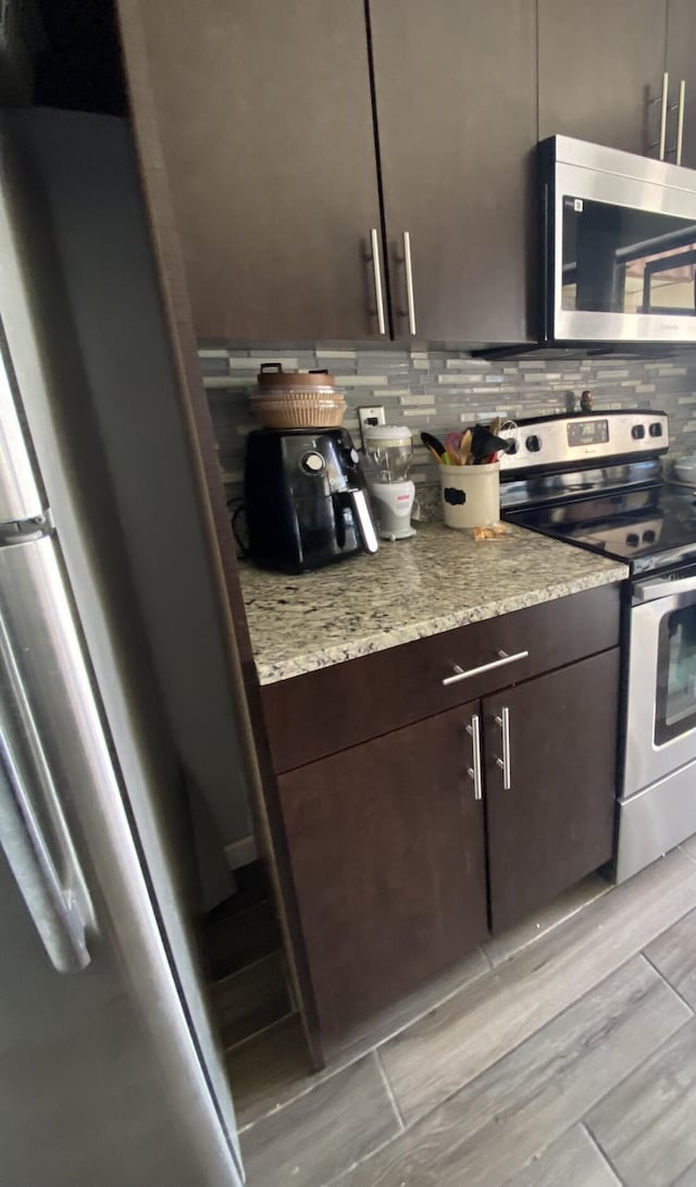 kitchen with decorative backsplash, stainless steel appliances, light stone countertops, and dark brown cabinets