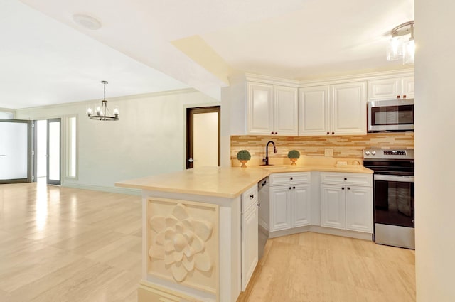 kitchen featuring a notable chandelier, kitchen peninsula, white cabinets, appliances with stainless steel finishes, and decorative backsplash