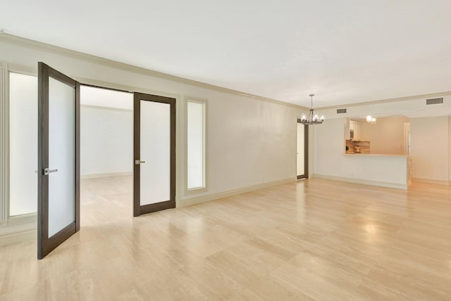 unfurnished living room with an inviting chandelier, light wood-type flooring, french doors, and ornamental molding