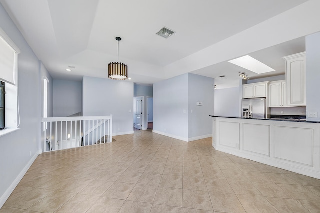 kitchen with stainless steel fridge, decorative light fixtures, light tile patterned floors, a skylight, and white cabinets