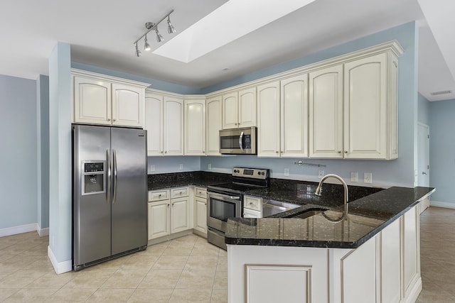 kitchen with dark stone countertops, a skylight, stainless steel appliances, kitchen peninsula, and sink