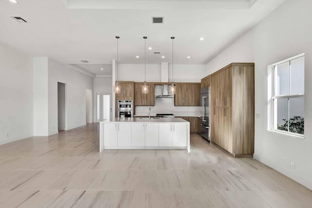 kitchen with sink, wall chimney range hood, stainless steel appliances, a center island with sink, and decorative light fixtures