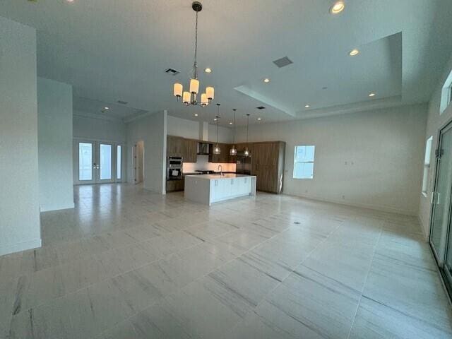 kitchen featuring an inviting chandelier, decorative light fixtures, an island with sink, built in fridge, and dishwasher