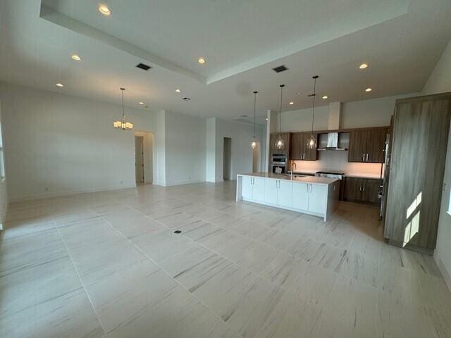 kitchen with hanging light fixtures, wall chimney exhaust hood, a center island with sink, and appliances with stainless steel finishes