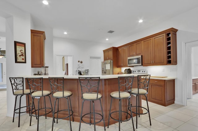 kitchen with kitchen peninsula, a kitchen breakfast bar, light tile patterned floors, and stainless steel appliances