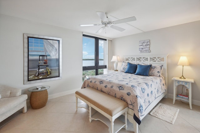 tiled bedroom featuring a water view, ceiling fan, and a wall of windows