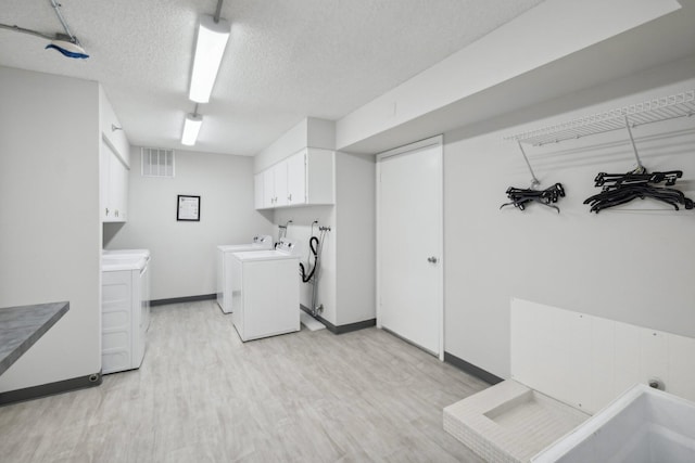 laundry area featuring light wood-type flooring, washer and dryer, a textured ceiling, and cabinets