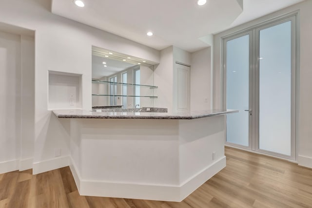 kitchen with light hardwood / wood-style floors, kitchen peninsula, and stone countertops