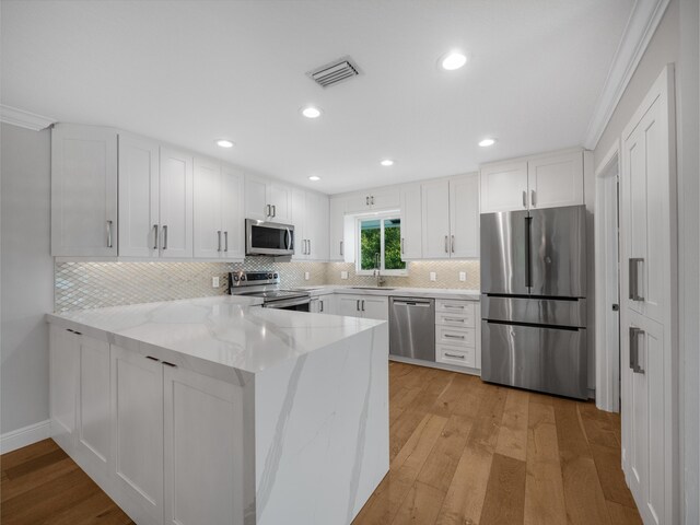 kitchen featuring white cabinetry, light hardwood / wood-style floors, light stone counters, kitchen peninsula, and stainless steel appliances