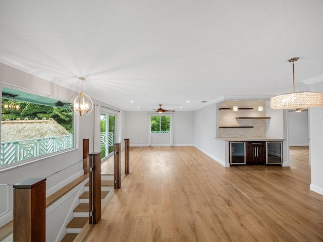 unfurnished living room featuring crown molding, light hardwood / wood-style flooring, beverage cooler, and ceiling fan with notable chandelier