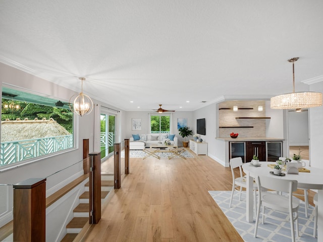 living room with ceiling fan with notable chandelier, ornamental molding, and light hardwood / wood-style flooring