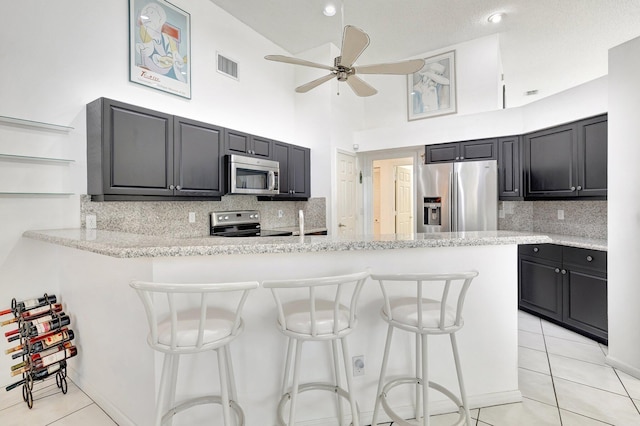 kitchen featuring kitchen peninsula, a high ceiling, stainless steel appliances, and light tile patterned floors