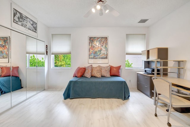 bedroom with a textured ceiling, light hardwood / wood-style flooring, a closet, and ceiling fan