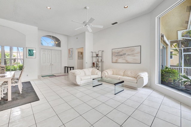 living room with ceiling fan, a towering ceiling, a textured ceiling, and light tile patterned floors