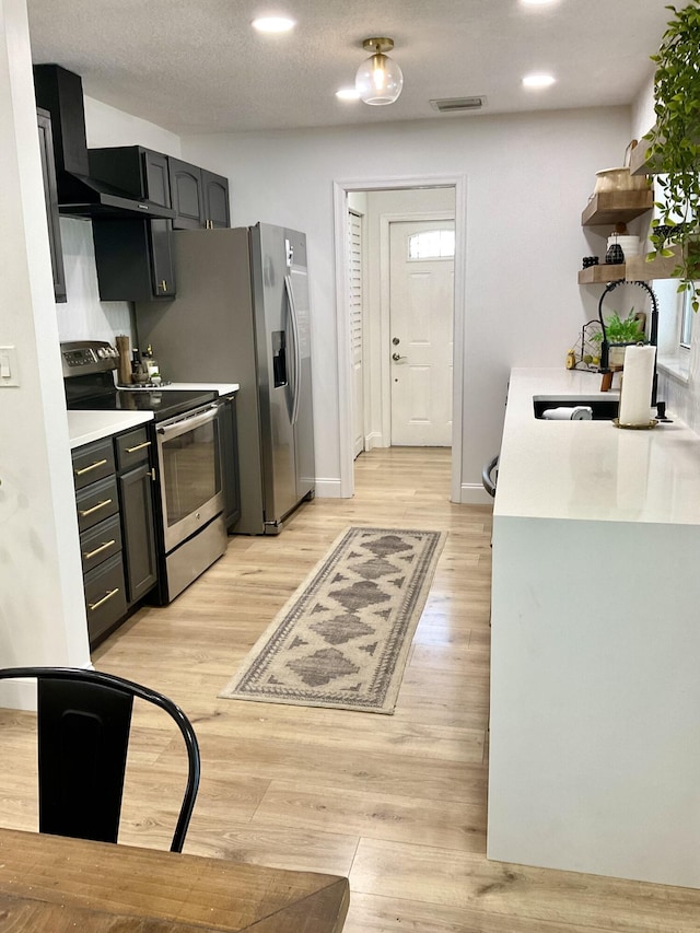 kitchen with a textured ceiling, light wood-type flooring, stainless steel appliances, and sink