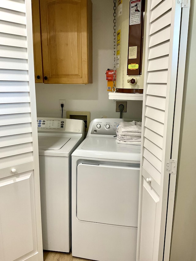 washroom with washing machine and clothes dryer, water heater, and cabinets