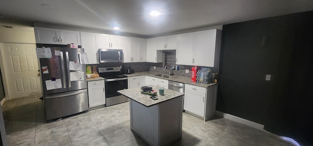 kitchen with light stone countertops, a center island, white cabinetry, stainless steel appliances, and sink