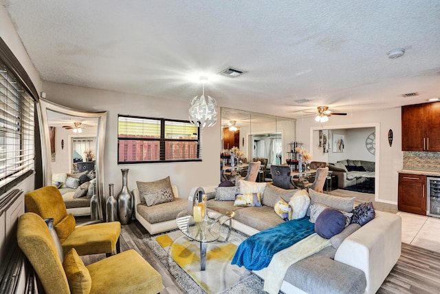 living room featuring wine cooler, a textured ceiling, an inviting chandelier, and a healthy amount of sunlight