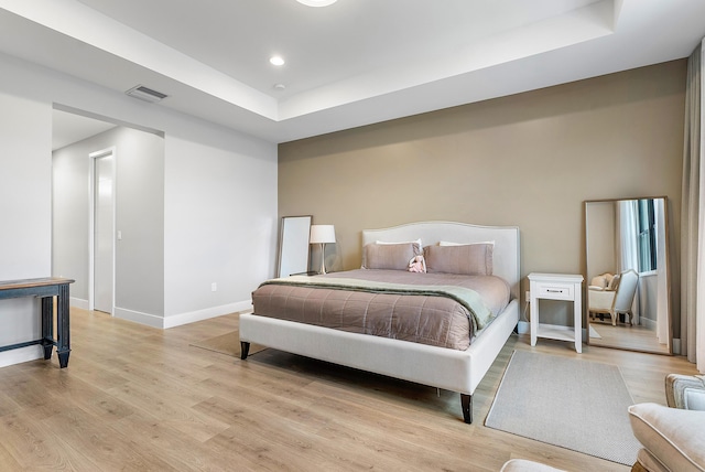 bedroom with a tray ceiling and light wood-type flooring