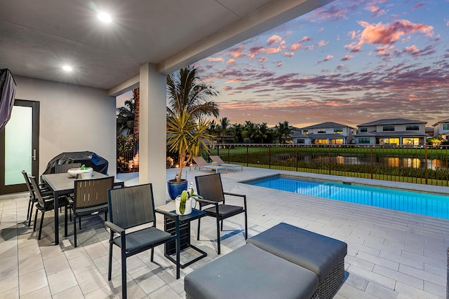 pool at dusk with a water view and a patio