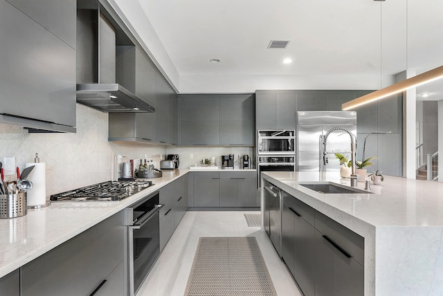 kitchen featuring pendant lighting, wall chimney range hood, stainless steel appliances, sink, and gray cabinetry