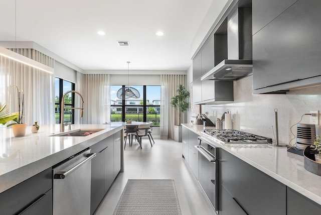 kitchen featuring stainless steel appliances, gray cabinetry, wall chimney range hood, pendant lighting, and sink