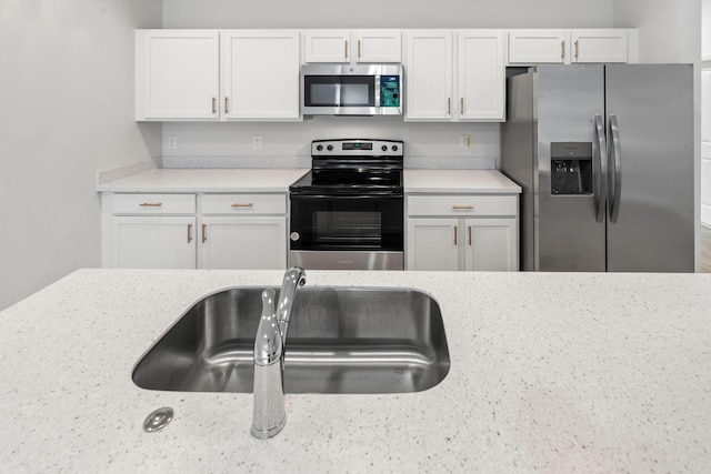 kitchen with white cabinetry, sink, light stone countertops, and appliances with stainless steel finishes