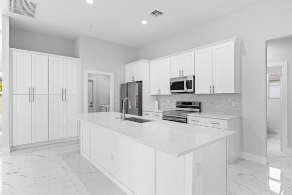 kitchen featuring a kitchen island with sink, sink, stainless steel appliances, and white cabinets