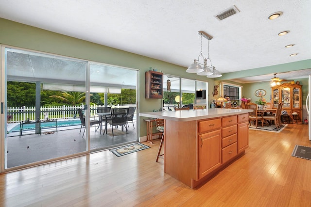 kitchen with ceiling fan, hanging light fixtures, a kitchen breakfast bar, light hardwood / wood-style flooring, and a kitchen island