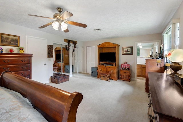 bedroom with a textured ceiling, two closets, ceiling fan, and light colored carpet