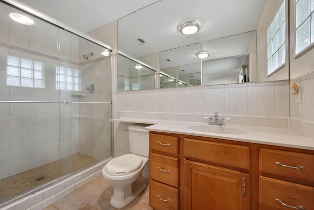 bathroom with vanity, a shower with door, tile patterned floors, toilet, and tile walls