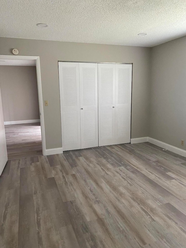 unfurnished bedroom with wood-type flooring, a closet, and a textured ceiling