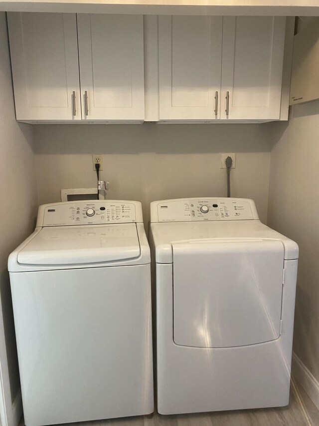 washroom with washing machine and clothes dryer, hardwood / wood-style floors, and cabinets