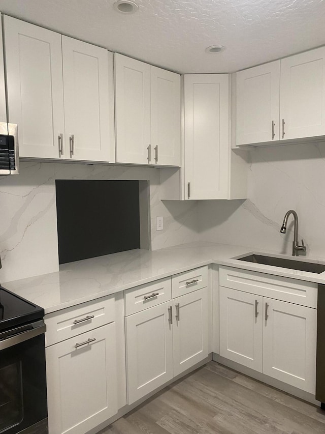 kitchen featuring black electric range oven, sink, tasteful backsplash, white cabinets, and light wood-type flooring