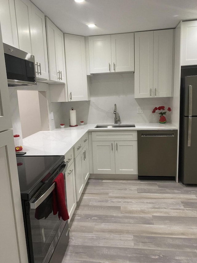 kitchen with sink, appliances with stainless steel finishes, light wood-type flooring, and white cabinetry